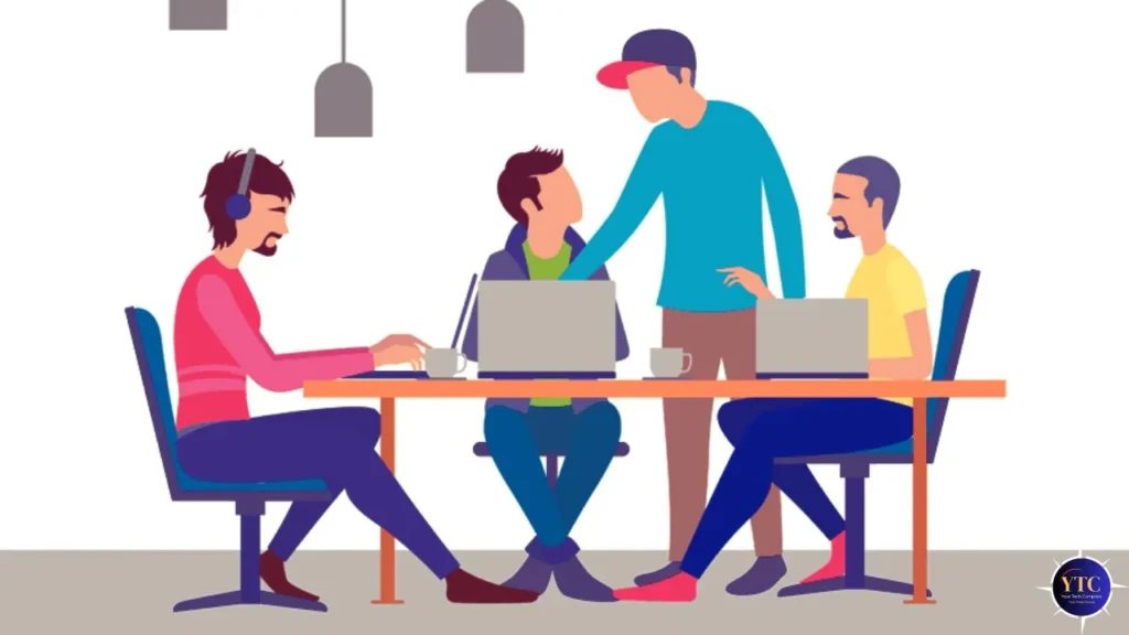 A flat-style illustration of four people collaborating around a shared desk: three seated with laptops (one wearing headphones), and one standing and gesturing toward the screen, depicting a modern, inclusive team workflow in a bright office setting.