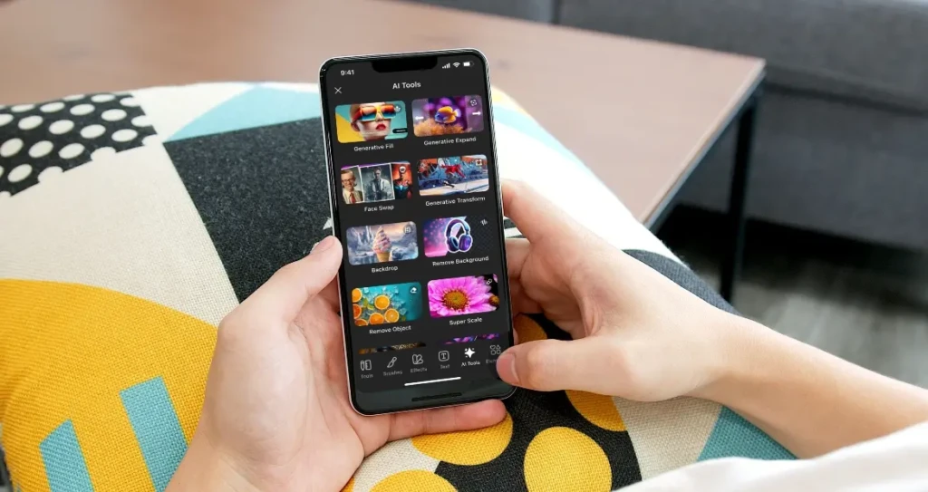 A person holding a smartphone on a patterned couch, navigating the “AI Tools” menu in CapCut, which includes options like Generative Fill, Face Swap, Remove Background, and Super Scale, illustrating accessible, on-device AI-powered video and photo enhancements.