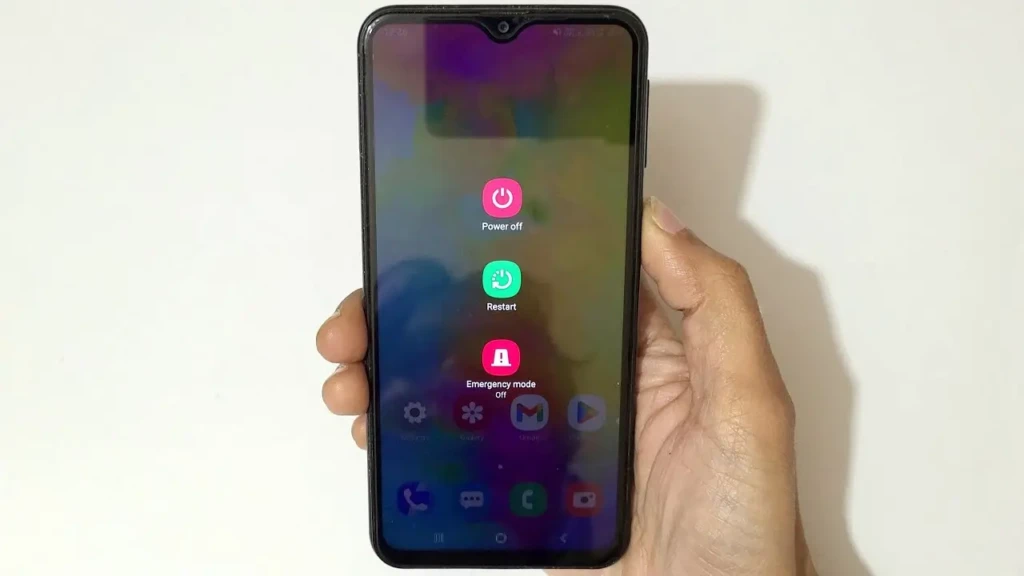 A hand holding an Android phone displaying the power menu with three options: “Power off,” “Restart,” and “Emergency mode,” each with distinct icons and labels, indicating a soft reset as a troubleshooting step for persistent app crashes.