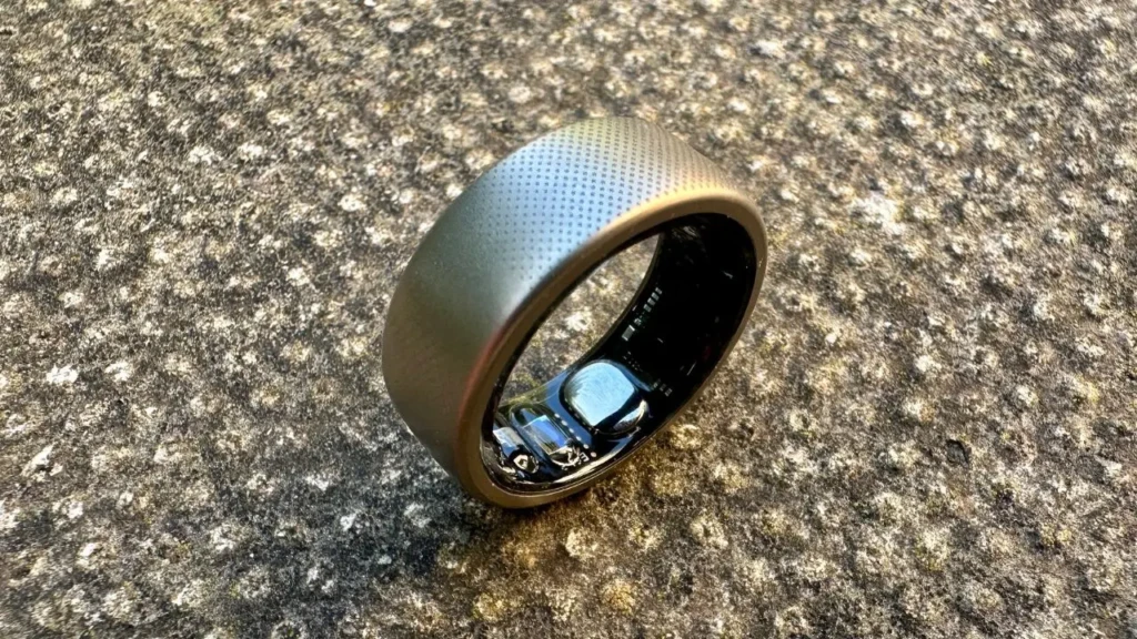 A matte-finish smart ring resting on a textured stone surface, with its inner electronics, including optical sensors and circuitry, visible through the open interior, emphasizing rugged durability and technical integration in a natural setting.