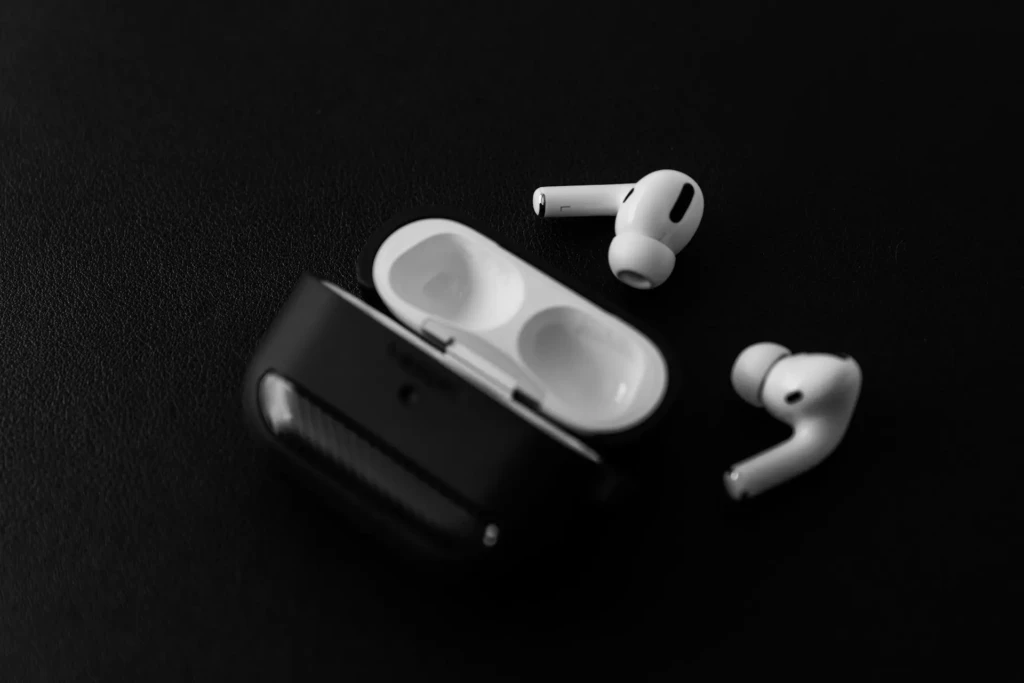 Black and white photo of wireless earbuds and an open charging case on a dark surface, conveying a sleek and modern tone.