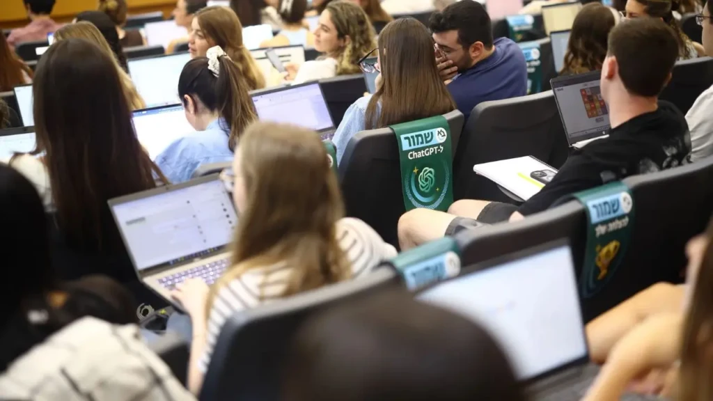 A classroom filled with students using laptops, viewed from behind. Each screen displays bright content, suggesting focused activity and engagement.