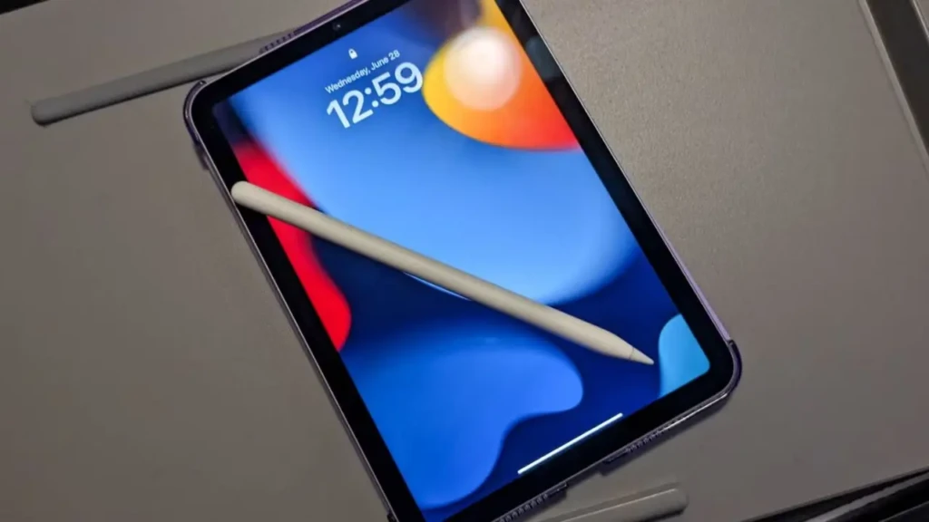 Tablet on a table displaying abstract colorful shapes on the screen, a digital pen resting diagonally across it, indicating creative or tech themes.