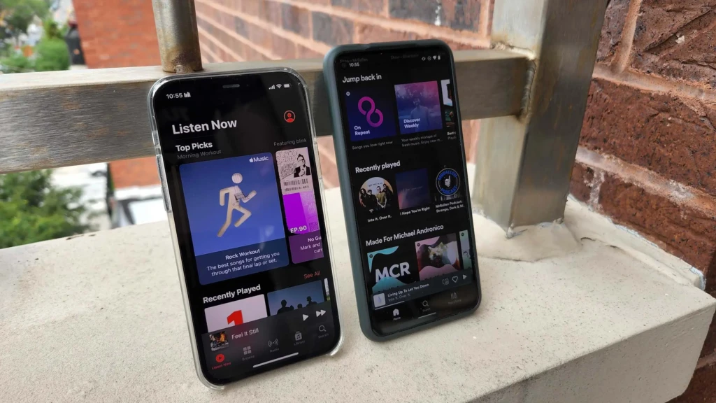 Two smartphones on a ledge display music apps, one showing Apple Music with workout playlists, the other featuring recently played songs.