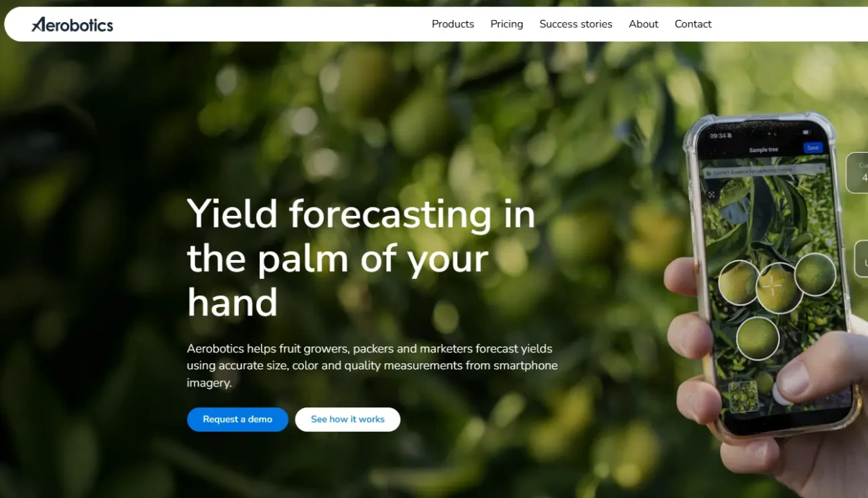 Close-up of a smartphone in a hand, displaying an app analysing fruit on a tree. Text overlay reads: 'Yield forecasting in the palm of your hand.' Lush green foliage in the background conveys technology and agriculture integration.