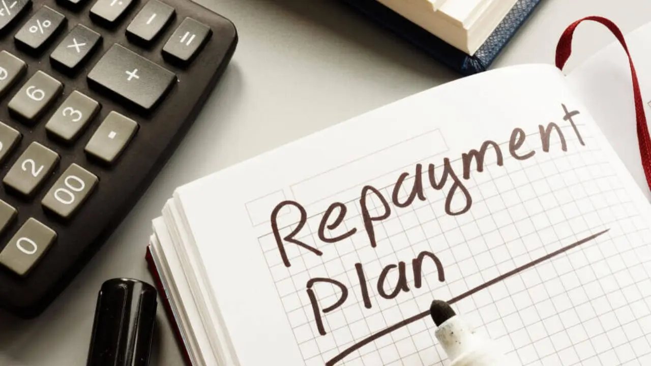 Open notebook with 'Repayment Plan' written on grid paper, beside a calculator and pen on a desk, suggesting budgeting or financial planning.