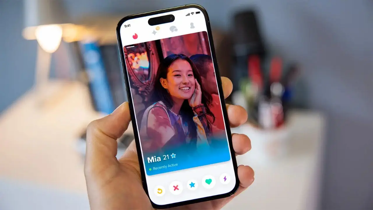 A hand holds a smartphone displaying a dating app profile. The screen shows a smiling woman named Mia, 21, with a colorful, vibrant background.