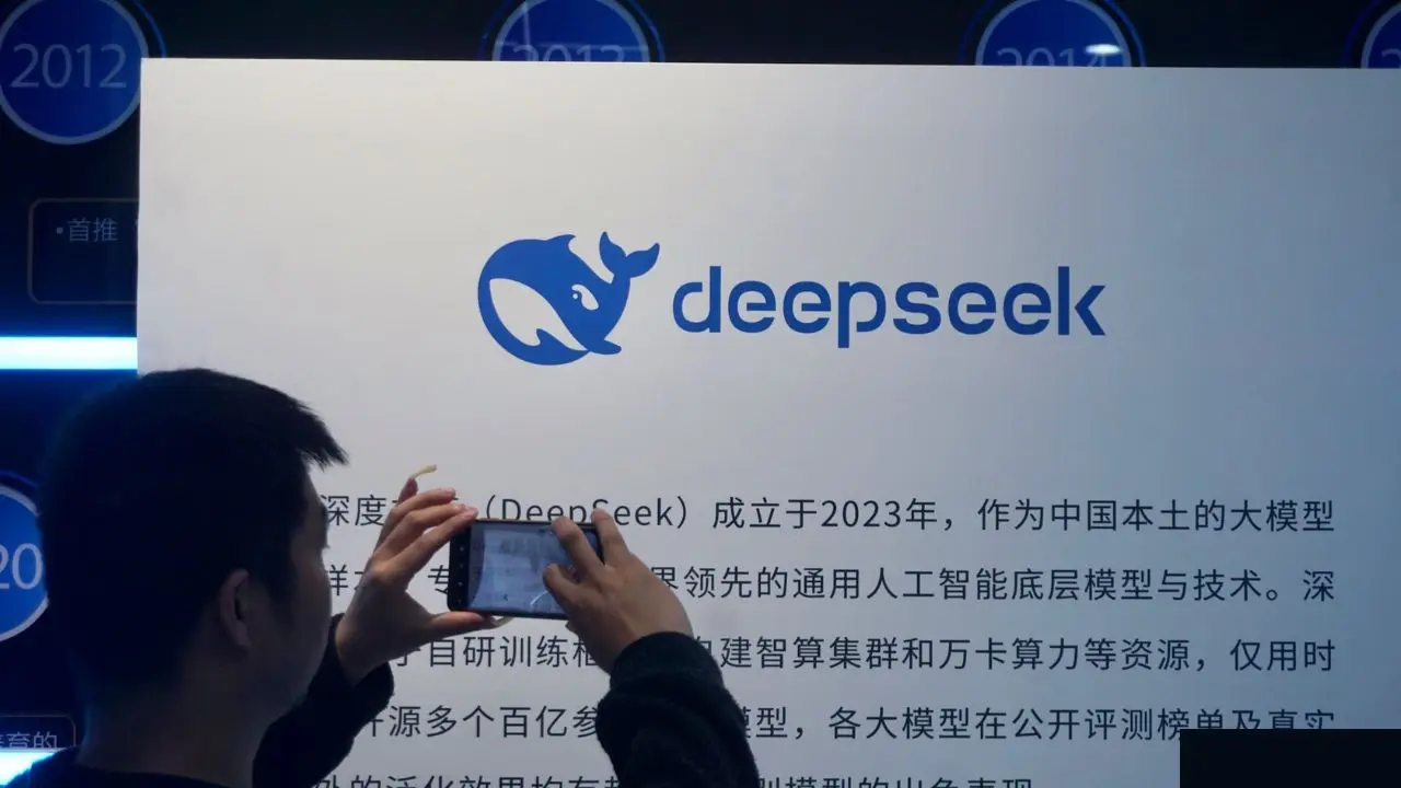A person takes a photo of a display board featuring the "deepseek" logo with a blue whale icon and Chinese text. The setting appears to be tech-related, conveying a sense of innovation.