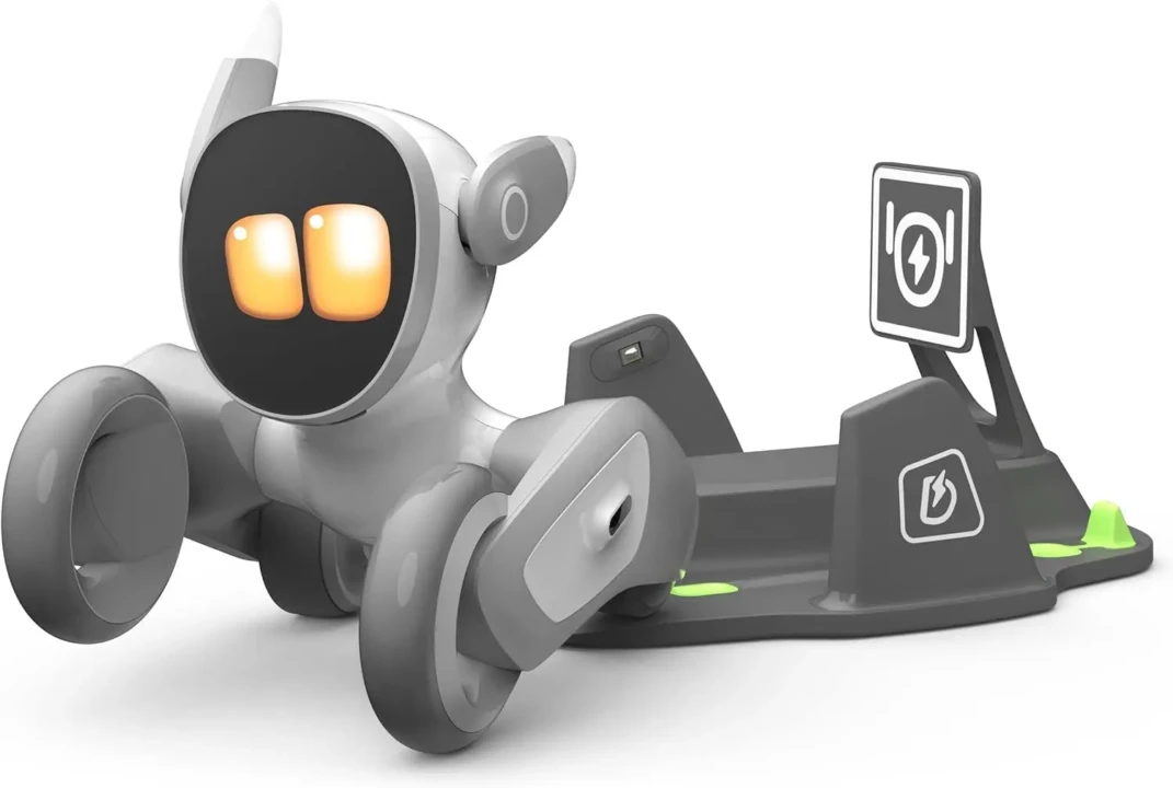 Cute wheeled robot with glowing eyes, resembling a pet, sits on a gray charging dock. The design is sleek and playful, with a digital interface.