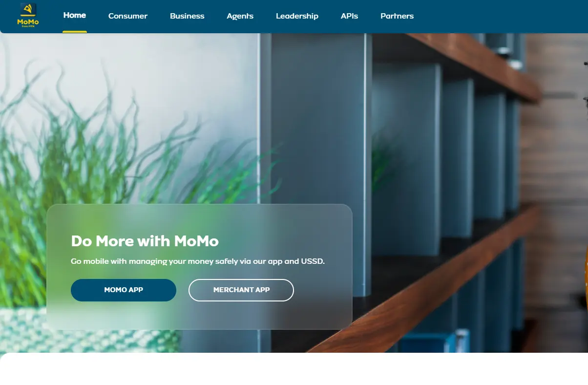 Homepage features a MoMo financial service banner with options for the MoMo and Merchant apps. Background shows modern shelves and green plants.