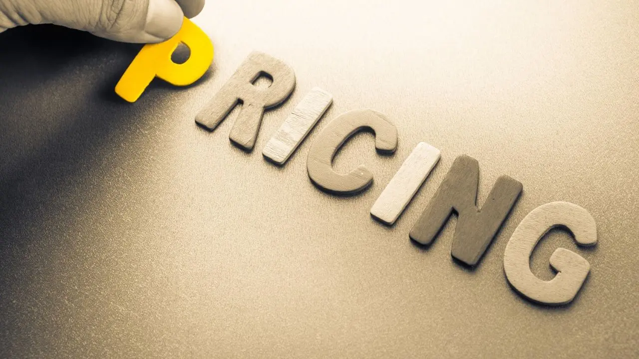 A hand places a yellow letter "P" in front of the word "RICING," forming "PRICING," on a textured surface. The tone is professional and creative.