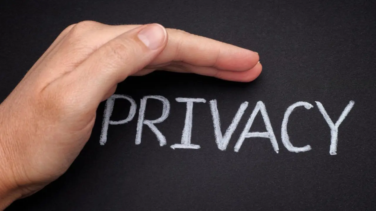 A hand hovers protectively over the word "PRIVACY" written in white chalk on a blackboard, symbolizing safeguarding privacy.