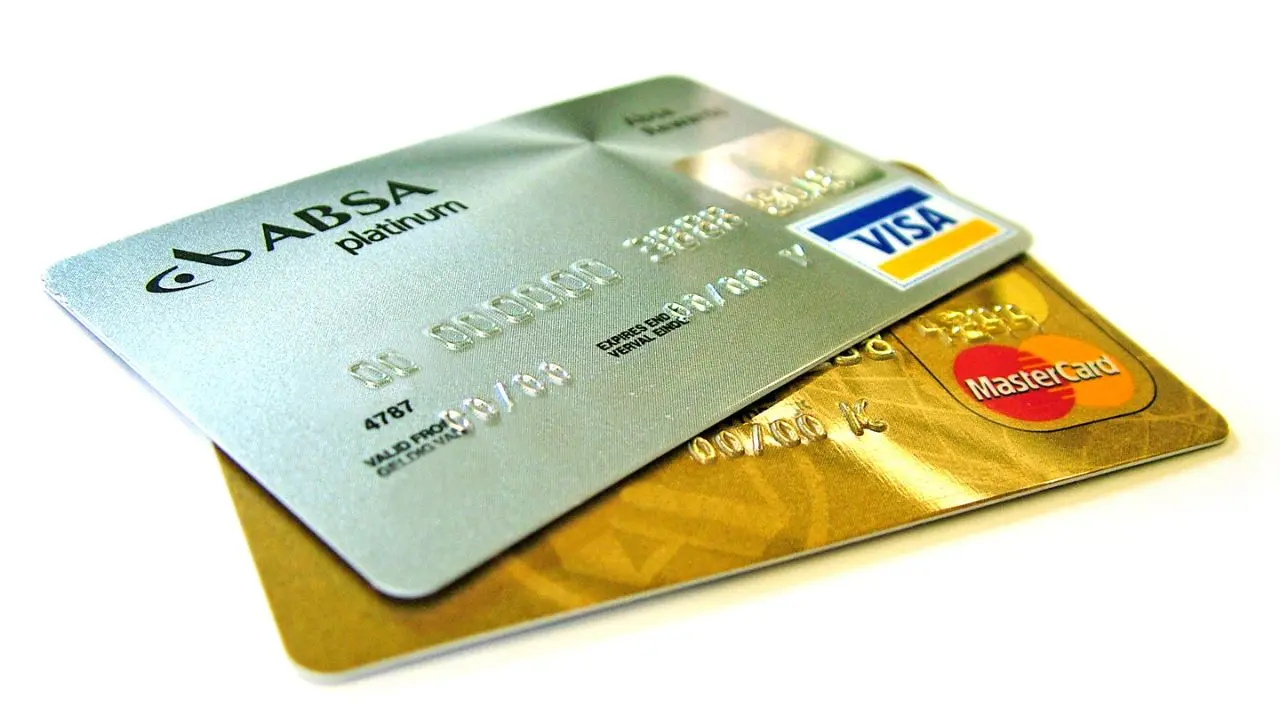 Two credit cards are overlapping; the top card is silver with embossed text and a Visa logo, and the bottom card is gold with a MasterCard logo. The image conveys themes of finance and credit.