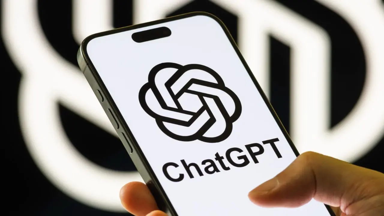 A hand holds a smartphone displaying the ChatGPT logo and text. The background features a blurred pattern, conveying technology and modernity.