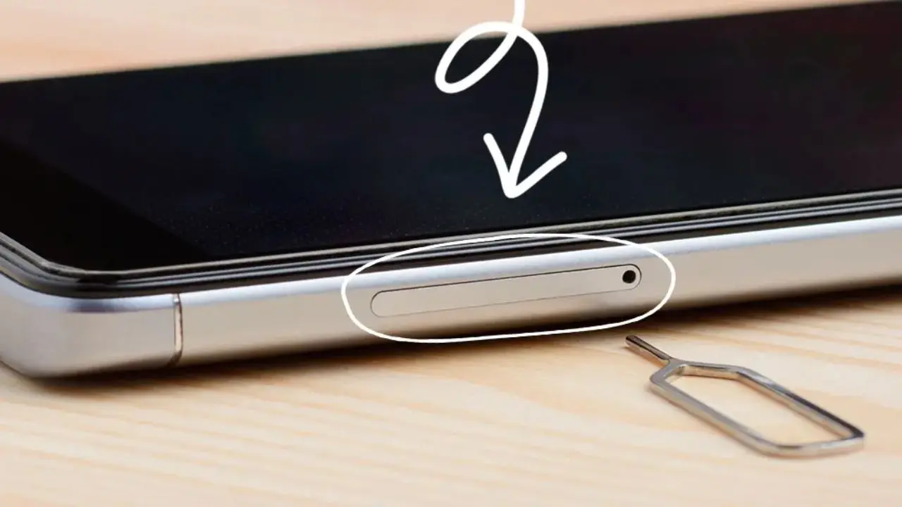 A smartphone lays face down on a wooden surface, showing the SIM card slot highlighted with a white arrow. A SIM ejector tool is nearby.