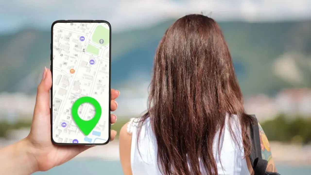 A person with long brown hair appears to be lost, standing outdoors with a scenic mountain view. A hand holds a smartphone showing a map and a large green location pin in the foreground.
