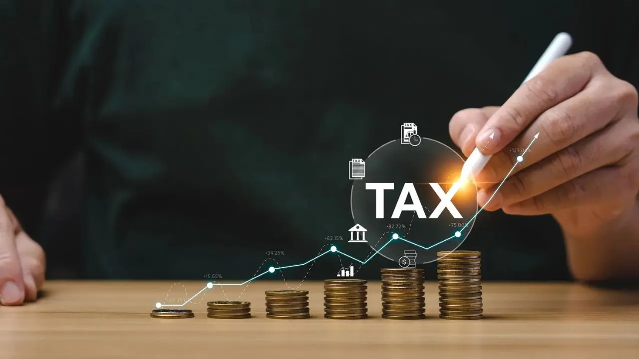 A hand holds a pen above stacked coins with upward trend lines, graphs, and icons, illustrating tax growth. The tone conveys financial planning.