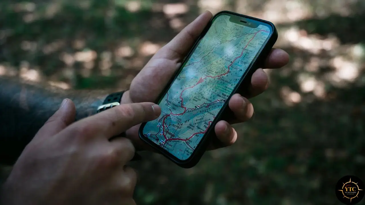 Hands holding a smartphone displaying a topographic map in a forest setting.