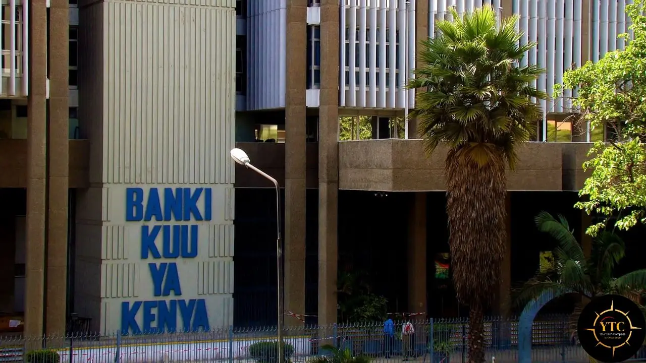 The Central Bank of Kenya building, Banki Kuu Ya Kenya, is shown with blue lettering alongside a tall palm tree and lush foliage.